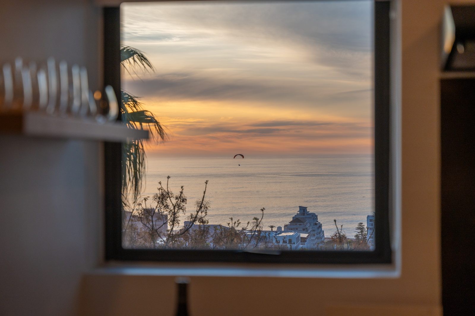 Sunset over the Atlantic framed by a window, with a paraglider above the sea