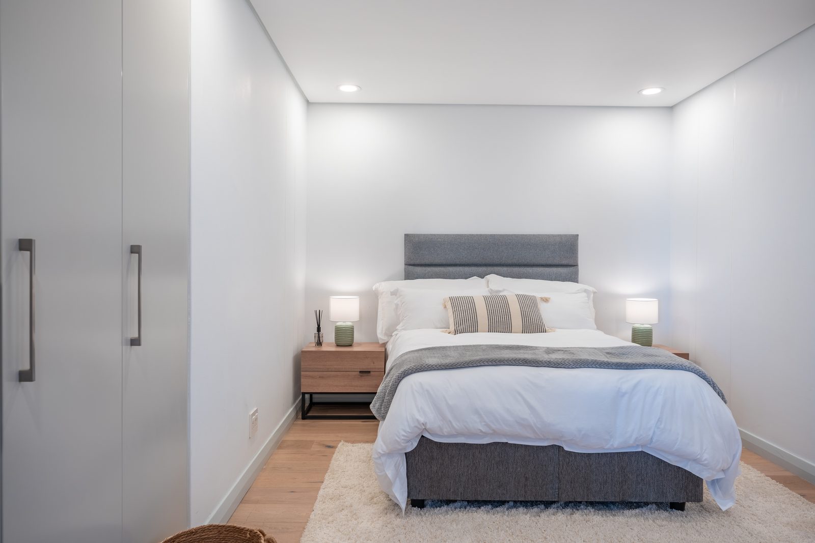 Second bedroom with a grey upholstered bed, bedside lamps and tall wardrobes