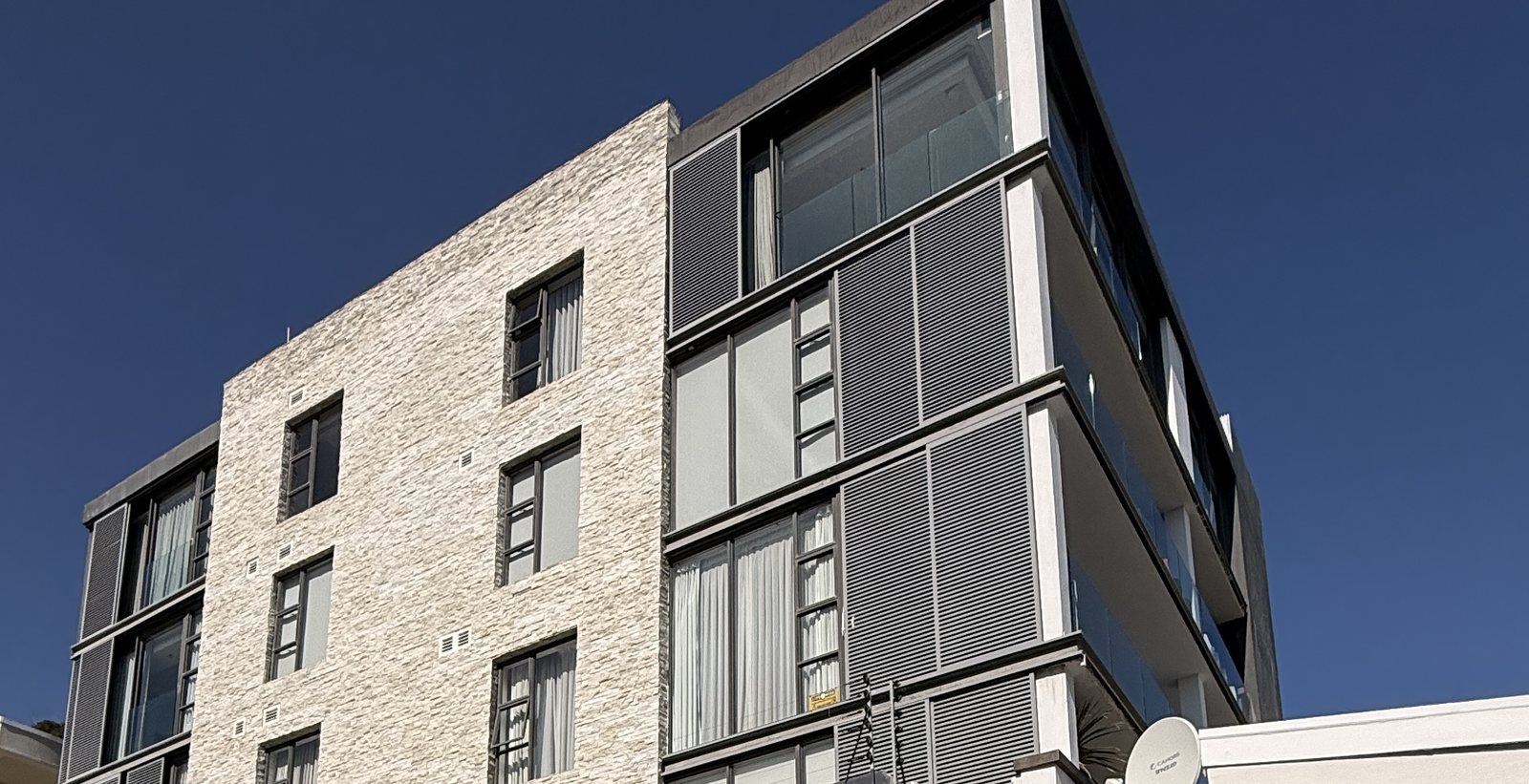 Stone-clad and louvred facades of the apartment building against a blue sky